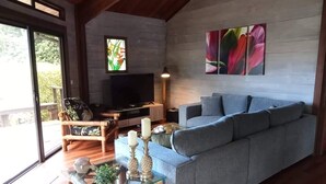 Un salon avec un canapé gris, une table basse en bois, un téléviseur et une grande fenêtre.