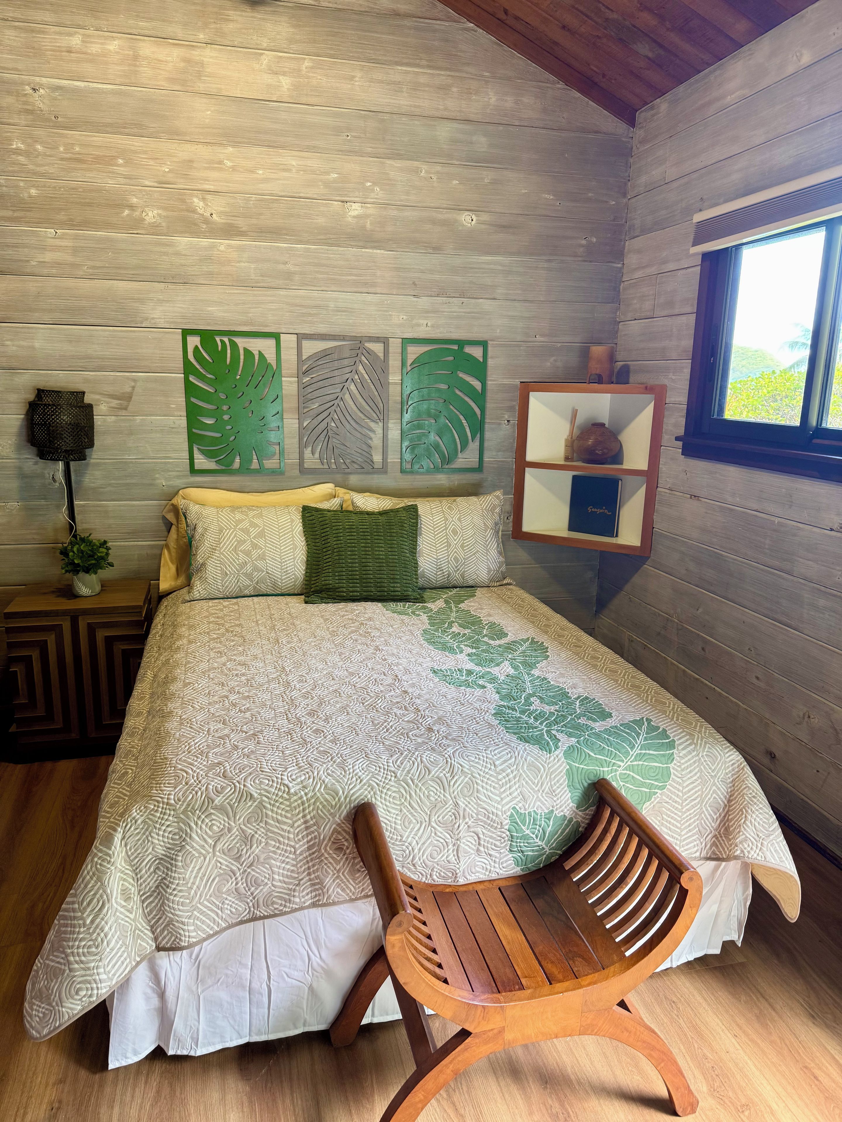 Ein Schlafzimmer einer Holzhütte mit einem Bett, einem Holzstuhl, einem Nachttisch, einer Wandlampe und einem Regal mit Dekoration.