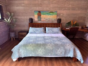 A bed with a blue patterned bedspread, a wooden headboard, and a painting of a beach scene on the wall. - Beautiful Private Home with Stunning Views of Opunohu Bay (Opunohu Bay)