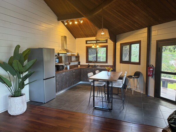 A modern kitchen with a central island, wooden cabinets, and a dining area with a table and chairs. - Beautiful Private Home with Stunning Views of Opunohu Bay (Opunohu Bay)