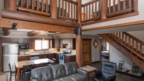 A spacious living area with a high ceiling, a wooden staircase, a dining area, and a kitchen. - Raven Cabin Vacation Rental (Valemount)