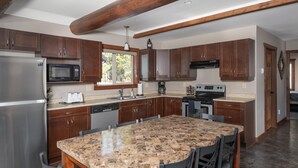 A modern kitchen with granite countertops, stainless steel appliances, and wooden cabinets. - Raven Cabin Vacation Rental (Valemount)