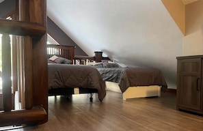 Un dormitorio tipo loft con dos camas, suelo de madera, una escalera y un armario.