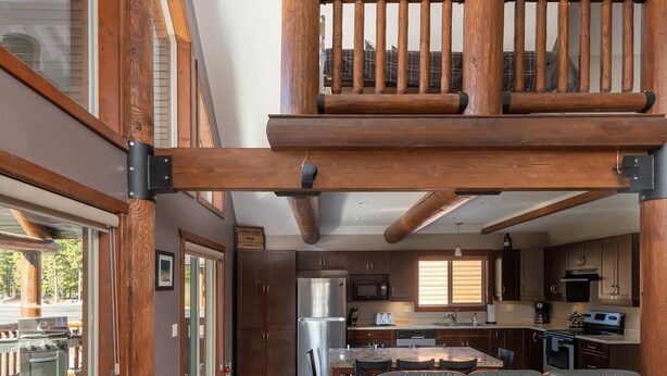 A spacious living area with a high ceiling, a balcony with wooden railings, and a kitchen in the background. - Raven Cabin Vacation Rental (Valemount)