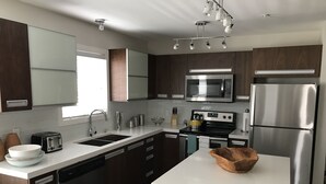 A modern kitchen with dark wood cabinets, stainless steel appliances, a white countertop, and a central island with a bowl. - Comfortable and Spacious 2BD, 2BA New Built Condo (Saskatoon)