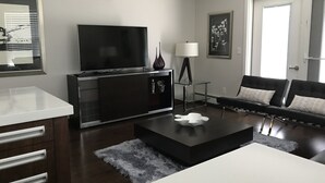 A modern living room with a flat-screen TV, a glass coffee table, a sofa, and a side table with a lamp. - Comfortable and Spacious 2BD, 2BA New Built Condo (Saskatoon)