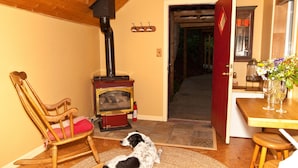 A cozy room with a wooden rocking chair, a pet dog, a fireplace, and a dining area with a vase of flowers. - Westover Bed and Breakfasts (Salt Spring Island)