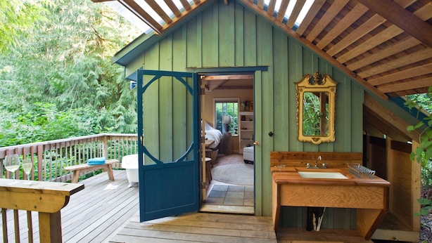 A wooden cabin with a balcony, a bathroom with a sink and mirror, and a door leading to a bedroom. - Westover Bed and Breakfasts (Salt Spring Island)
