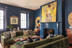 A cozy living room with a green sofa set, a fireplace, and artwork on the walls. - Casa Zoë | Grand Sparrow House (Charleston)