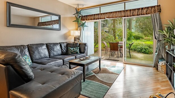 Ein Wohnzimmer mit einer schwarzen Ledersofa, einem Glastisch und Blick auf einen Garten durch eine Schiebetür.