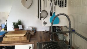 Uma cozinha com tábua de corte de madeira, pia e diversos utensílios pendurados na parede.