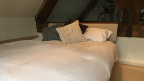 Quarto com teto inclinado, cama com roupa de cama branca e várias almofadas.