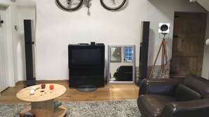 Sala de estar com uma bicicleta pendurada, televisão, tripé e sofá de couro.
