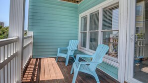 Een overdekte veranda met blauwgroene bekleding, witte relingen en twee lichtblauwe Adirondack-stoelen.