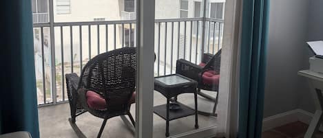 A balcony with wicker chairs and a table, a sliding glass door, and a view of a building with balconies.