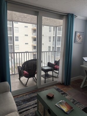 A balcony with wicker chairs and a table, a sliding glass door, and a view of a building with balconies.