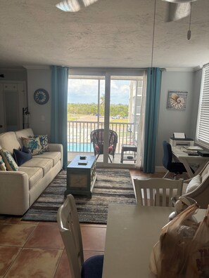 A living room with a sofa, coffee table, and a view of a pool and building.