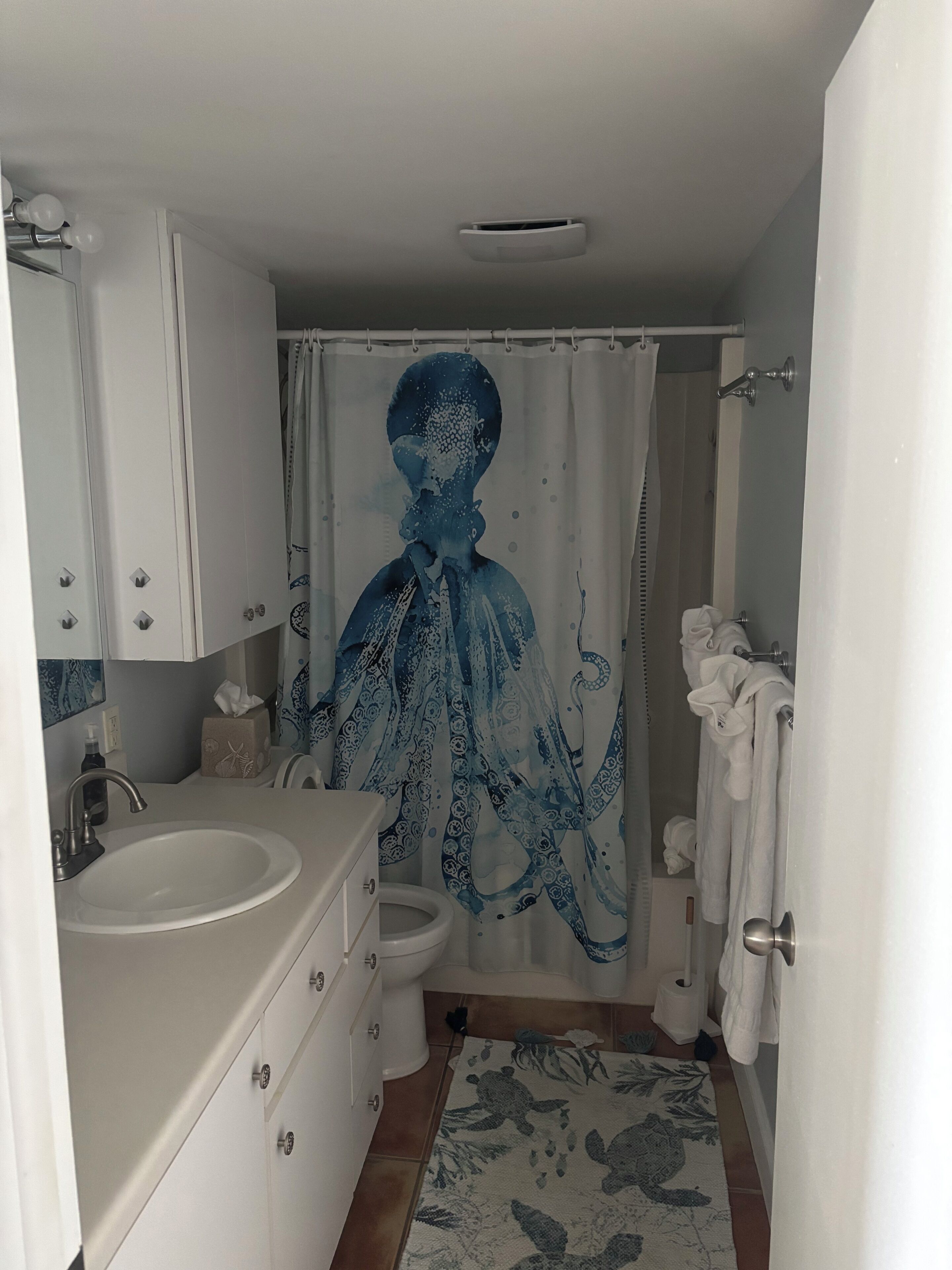 Un baño con lavamanos, inodoro y cortina de ducha con motivos de pulpo.
