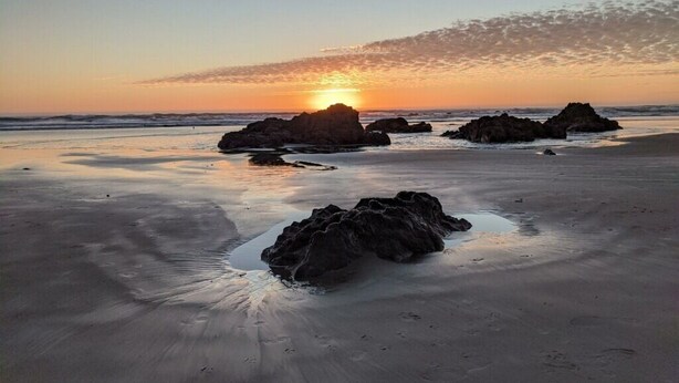 Una playa con rocas grandes y una puesta de sol al fondo.