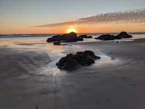 A beach with large rocks and a sunset in the background.
