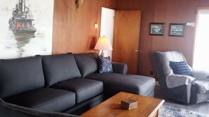 Una sala de estar con un sofá negro, una mesa de centro de madera y un cuadro de un barco en la pared.