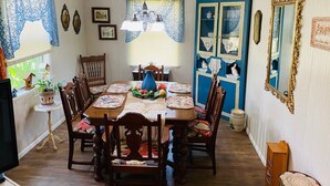 A dining room with a wooden table set for four, surrounded by chairs. There is a chandelier hanging from the ceiling, a blue cabinet with glass doors, and a large mirror with an ornate frame.