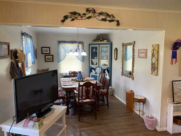 Un coin repas avec une table et des chaises en bois, un téléviseur posé sur un meuble, et un buffet bleu agrémenté d’objets décoratifs.