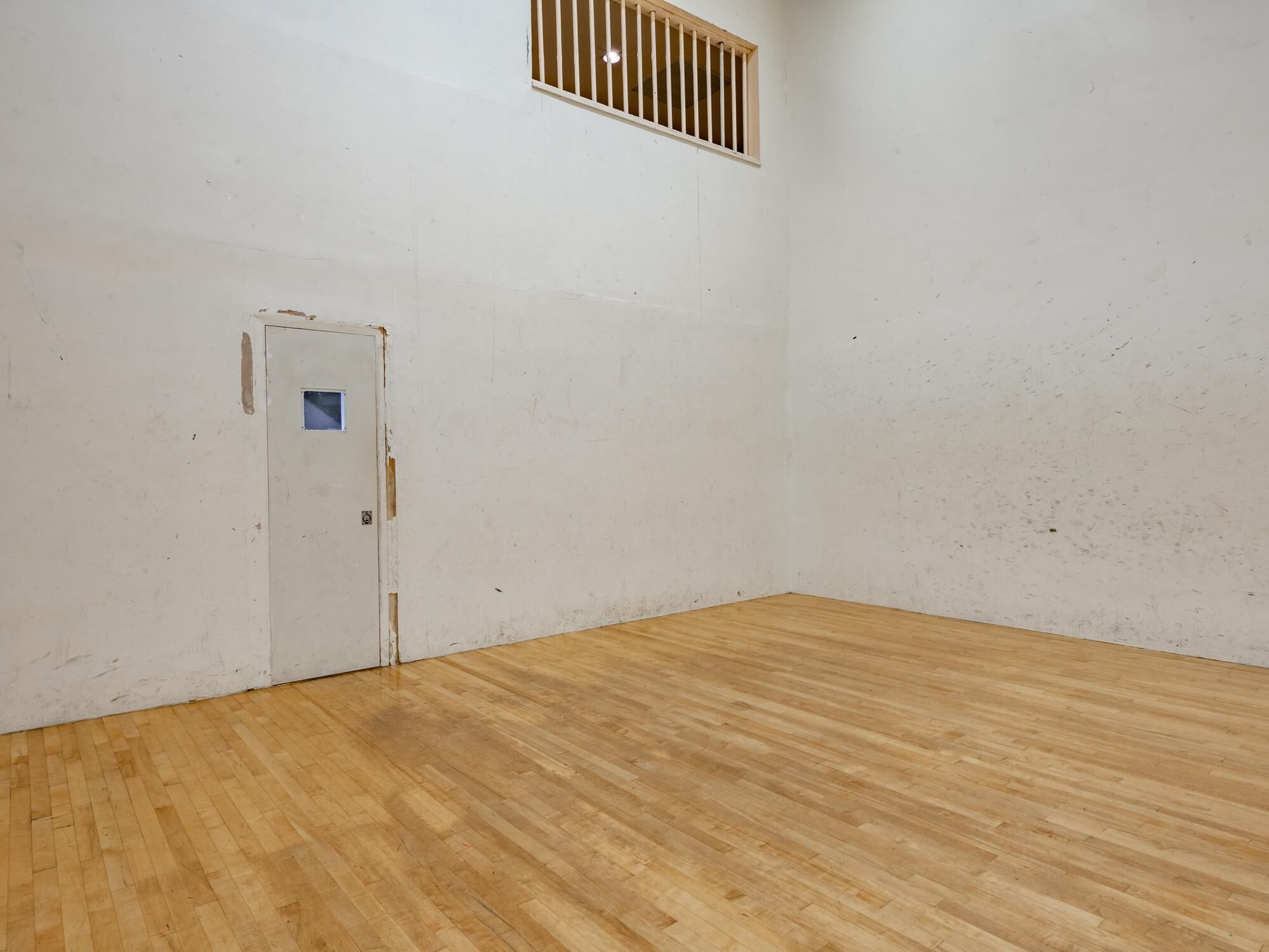 Une pièce avec un plancher en bois, un mur blanc et une porte dotée d’une petite fenêtre.