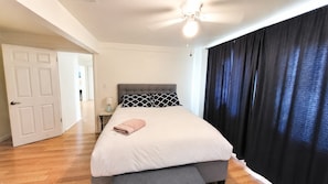 A bedroom with a bed, a nightstand, a ceiling fan, and a door leading to another room.