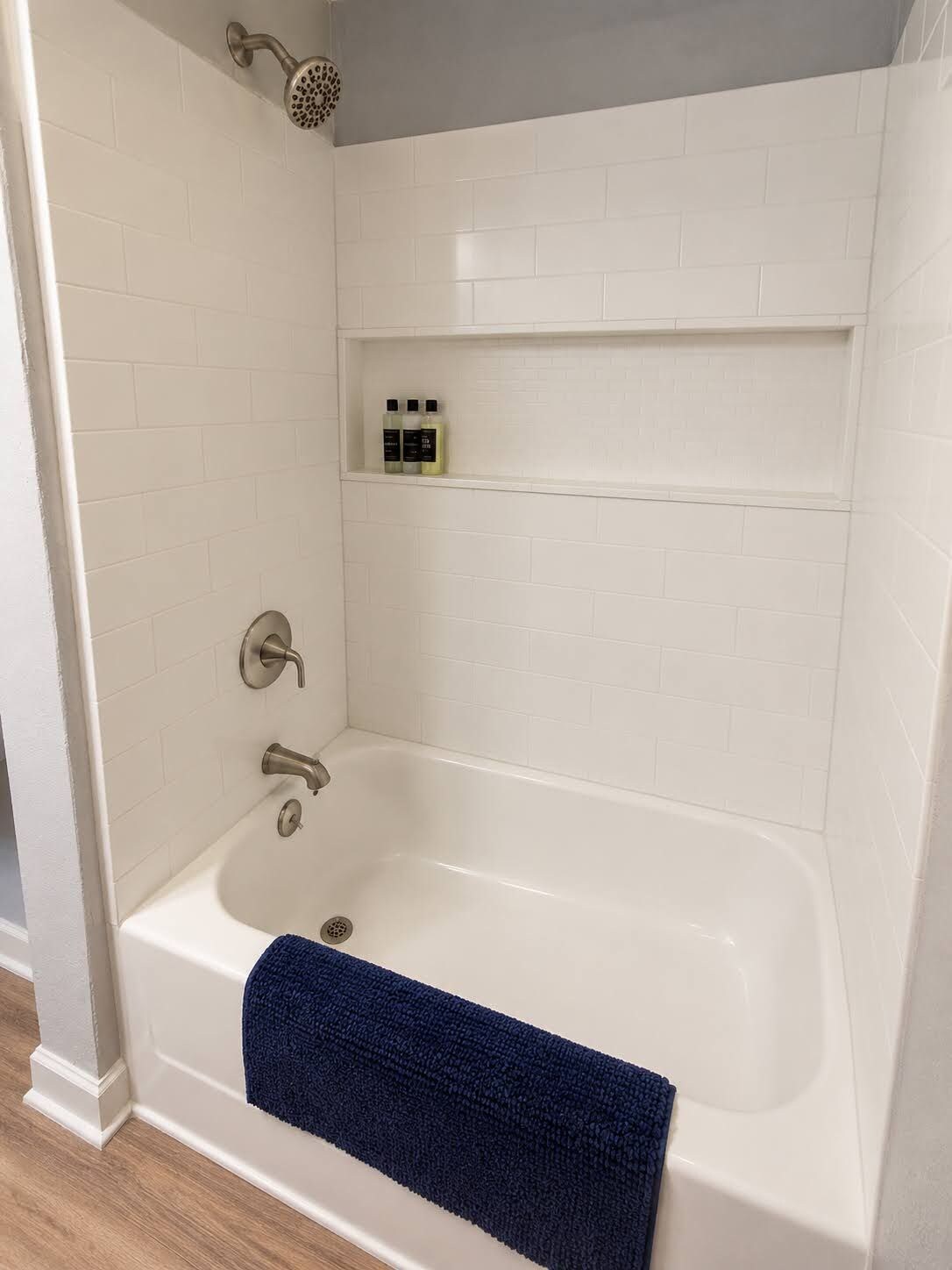 Et badeværelse med et hvidt badekar, brusehoved og en hylde med toiletartikler.