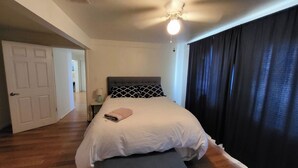 A bedroom with a bed, a nightstand, a lamp, a ceiling fan, and a door leading to another room. - 2BR 1BA Condo in Roosevelt Row Arts District (Phoenix)