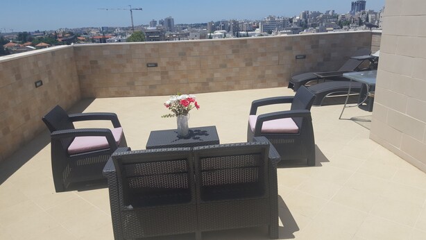 Eine Dachterrasse mit Korbmöbeln, einem Tisch mit Blumen und Blick auf die Stadt.