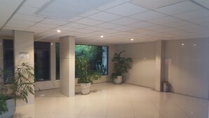 Eine großzügige Lobby mit Fliesenboden, großen Fenstern und Blick auf Grünflächen sowie einigen Blumentöpfen.