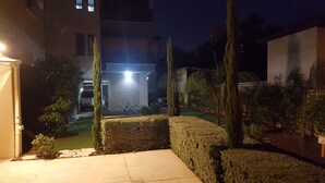 Ein Nachtblick auf eine Wohngegend mit einer gut beleuchteten Einfahrt, ordentlich geschnittenen Hecken und einem gepflasterten Weg, der zu einem Gebäude führt.