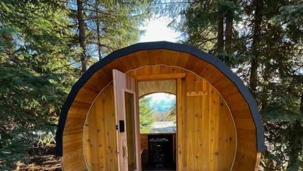 Una cabana de fusta amb disseny circular, amb dues bances i una porta que dona a un espai interior.