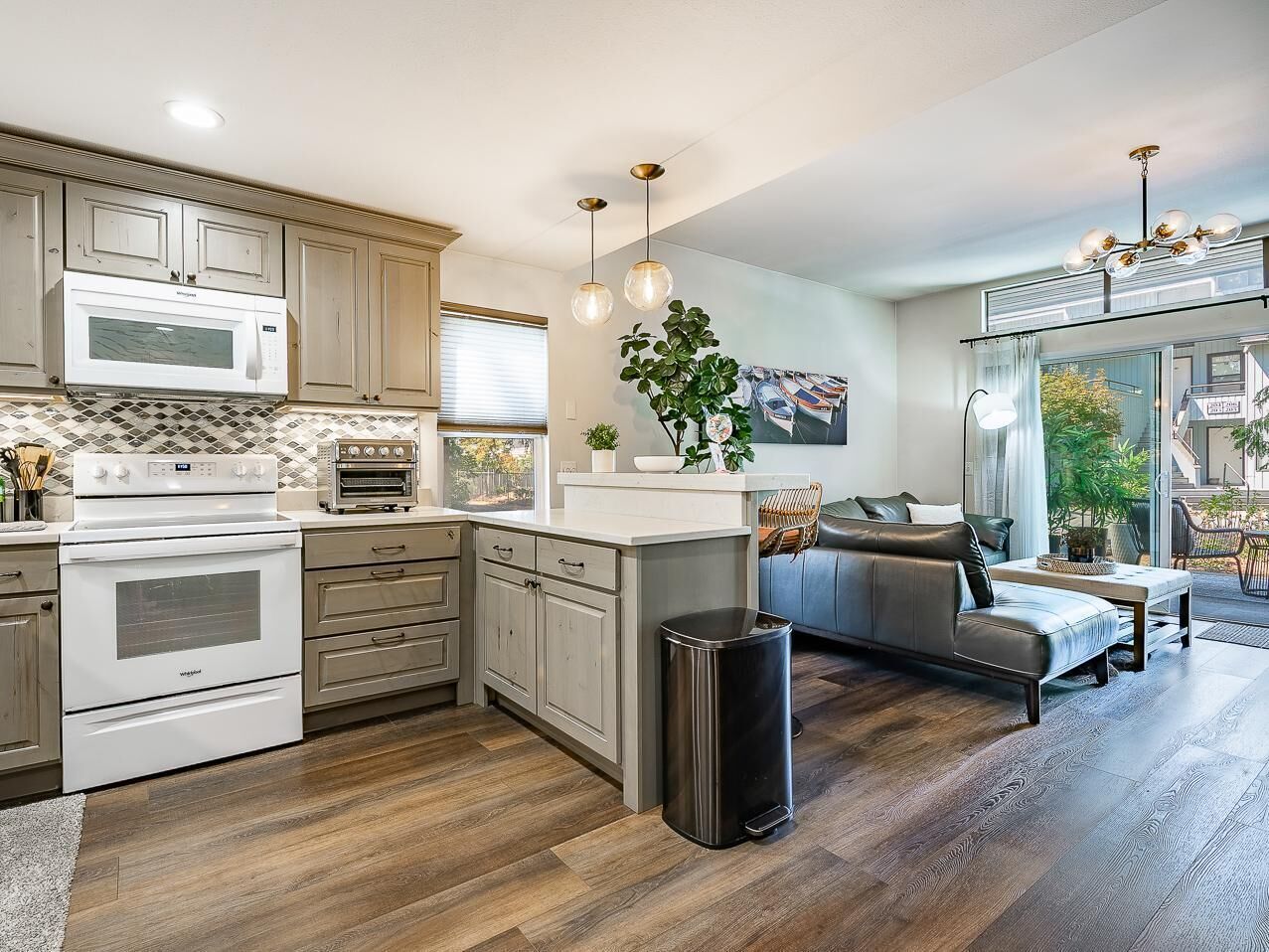 A modern kitchen with built-in appliances, a dining area with a sofa, and a view of the outdoors.