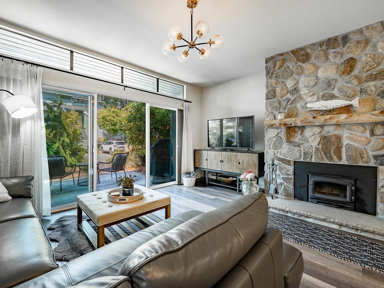A modern living room with a stone fireplace, leather sofas, a television, and a large sliding glass door leading to an outdoor area.
