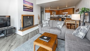 A modern living room with a sofa, coffee table, and TV. A kitchen is visible in the background. - JL 1112: Spectacular View, Steps to the beach, Free Wi-fi. (Birch Bay)