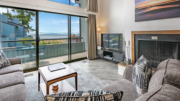 A spacious living room with a large window, a fireplace, and a television. - JL 1112: Spectacular View, Steps to the beach, Free Wi-fi. (Birch Bay)