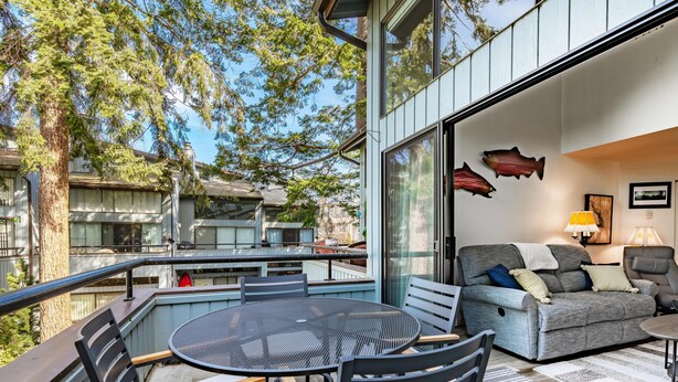 Un patio al aire libre con una mesa redonda y sillas, un sofá gris, y una zona de comedor con una parrilla.
