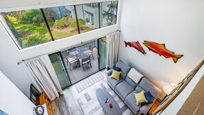 Una sala de estar moderna con un amplio ventanal que da a un patio exterior, un conjunto de sofás, una mesa de centro y decoraciones de peces montadas en la pared.