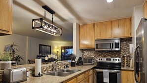 A modern kitchen with granite countertops, stainless steel appliances, wooden cabinets, and a backsplash.