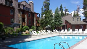 A swimming pool with lounge chairs and umbrellas, surrounded by buildings with balconies and trees.
