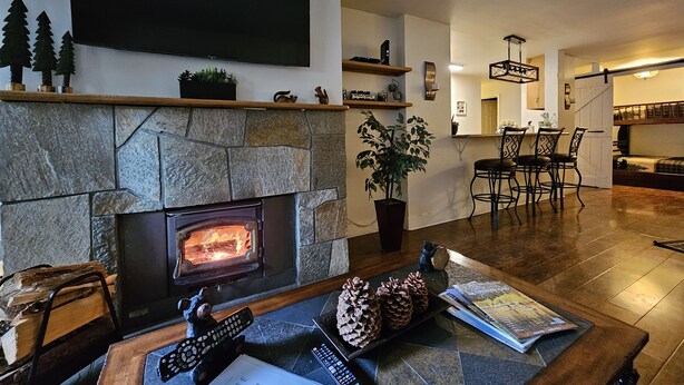 A cozy living room with a stone fireplace, a flat-screen TV, and a dining area with chairs and a table.