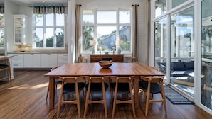 Un vaste espace dédié à la salle à manger, avec une table et des chaises en bois, de grandes fenêtres ornées de rideaux et une vue sur l’extérieur.