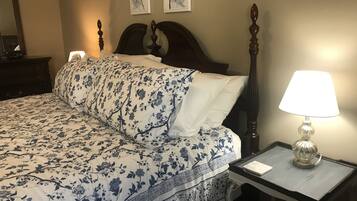 Una cama bien tendida con una colcha y almohadas estampadas con motivos florales, una mesita de noche con una lámpara y un cuadro en la pared.