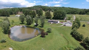 A large pond surrounded by well-maintained grass and trees, with a house and a small building nearby. - Beautiful rural setting cottage (Galax)