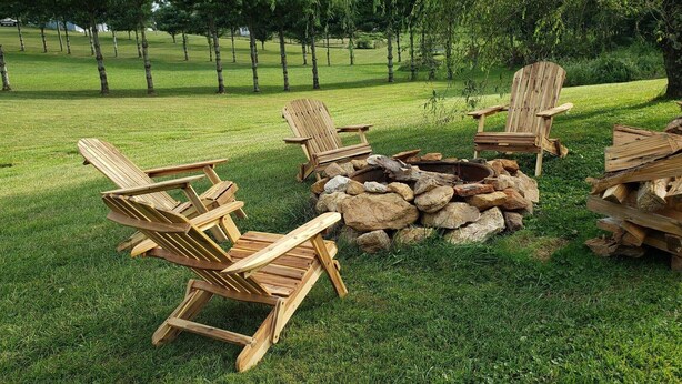 A grassy outdoor area with wooden Adirondack chairs arranged around a fire pit. - Beautiful rural setting cottage (Galax)
