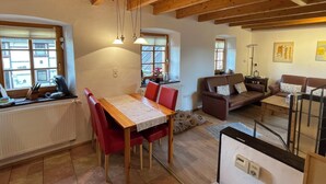 A spacious living area with a wooden ceiling, a dining table with red chairs, a sofa, and a coffee machine.