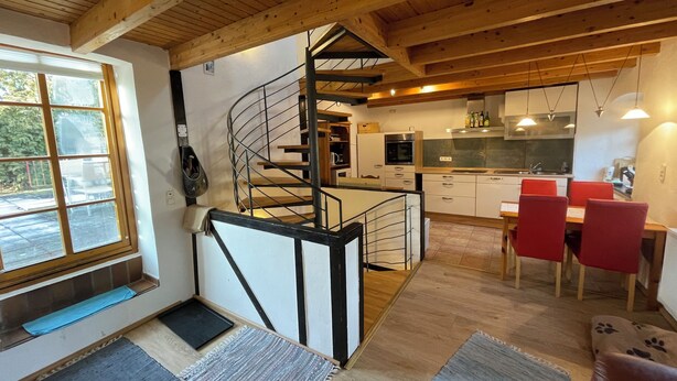 A modern interior with a spiral staircase, wooden beams, a kitchen, and a dining area with red chairs.